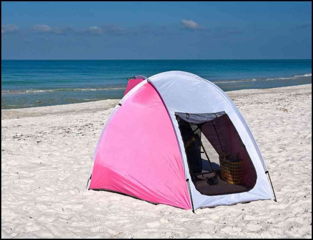 A pink and white baby tent set up by the beach